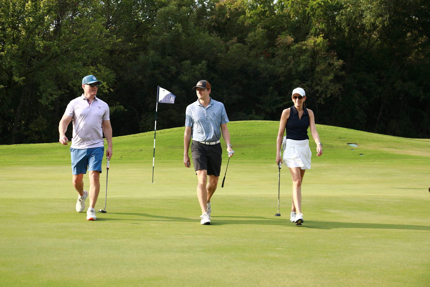 Three players walking off a green past a Cowboys flag