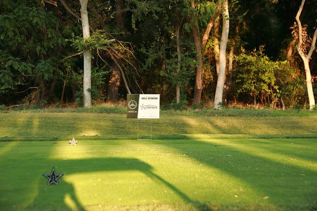 A hole sponsor sign on a tee box beside a Cowboys star tee marker