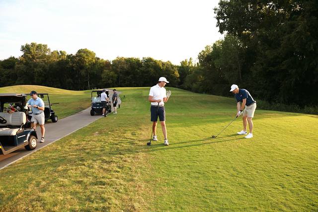 A group teeing off with carts parked along the path