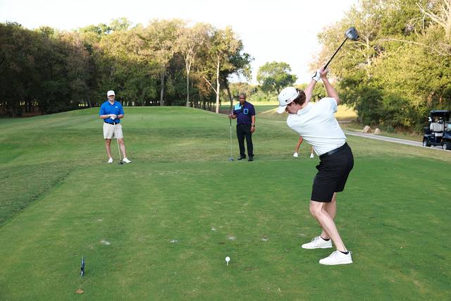 A player at the top of the backswing on a tee box while two playing partners watch