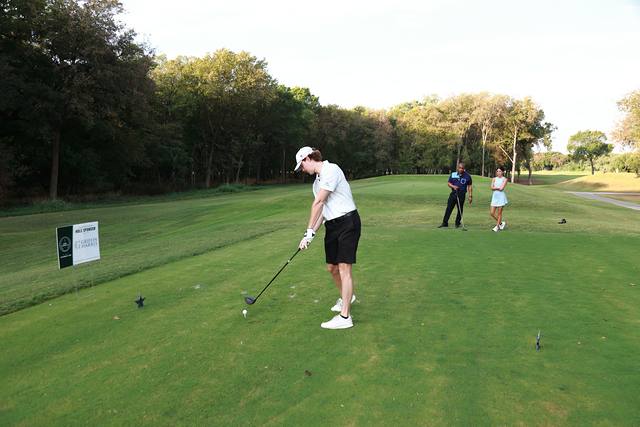 A player teeing off as his group watches from down the fairway
