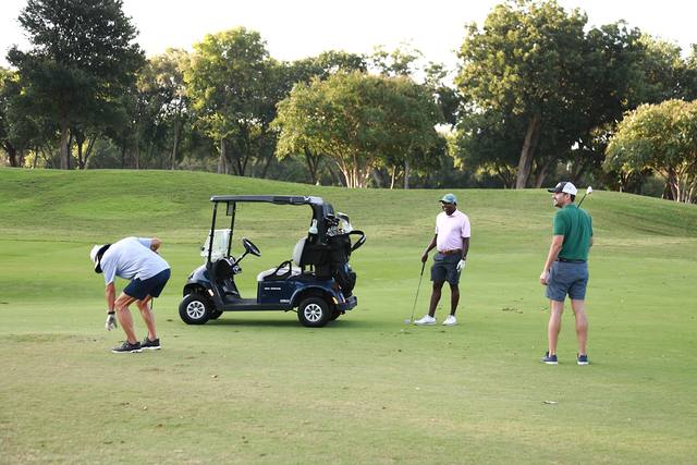 A player chipping beside his cart while his partners watch