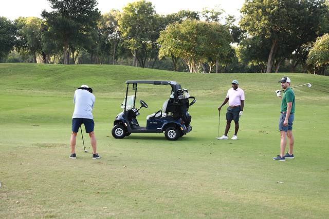 A player chipping toward the green while two partners wait by the cart