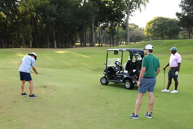 A player chipping beside his cart while his partners look on