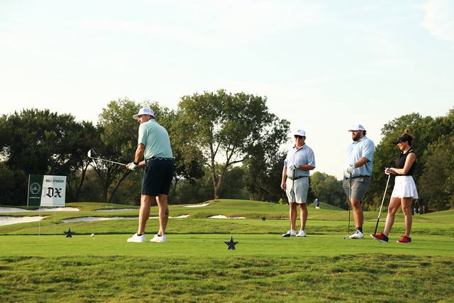 A group on a tee box beside The Dallas Express hole sponsor sign