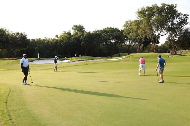 Four players spread across a green beside a bunker