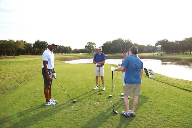 Three players talking on a tee box beside a pond
