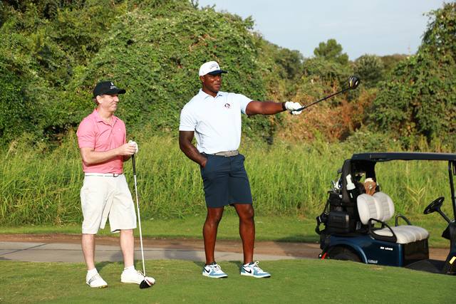 Two players laughing on a tee box beside their cart