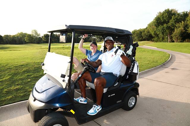 Two players waving from their cart on the cart path
