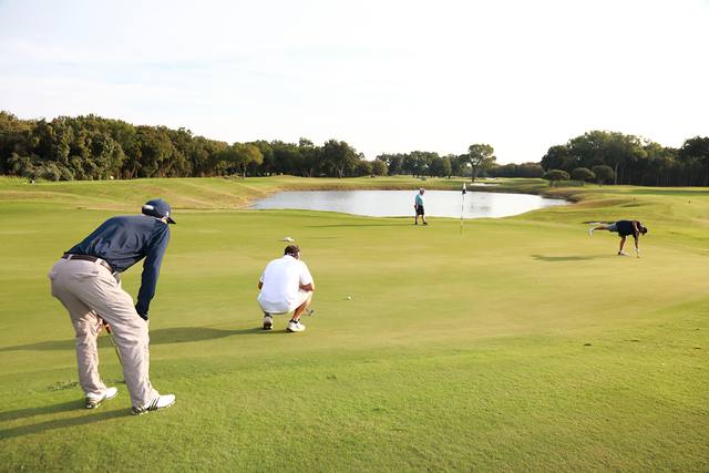 A player reading a putt across a green with a pond behind it