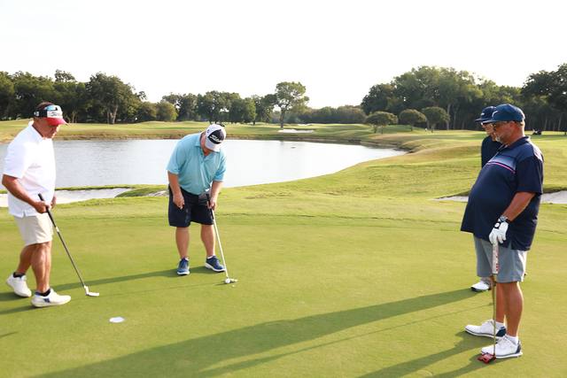 Three players on a green with a pond behind them