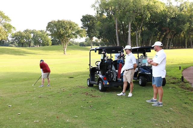 A player chipping while two partners wait by the carts
