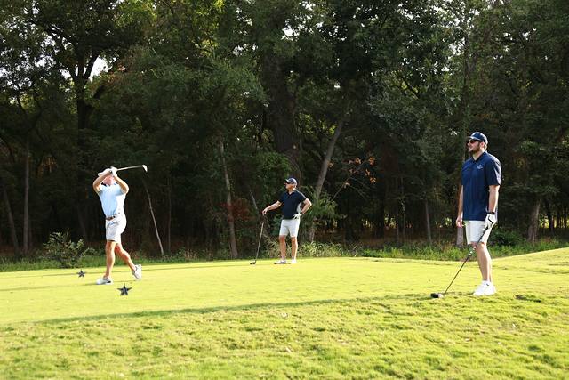 A player finishing his swing on a tree lined tee box