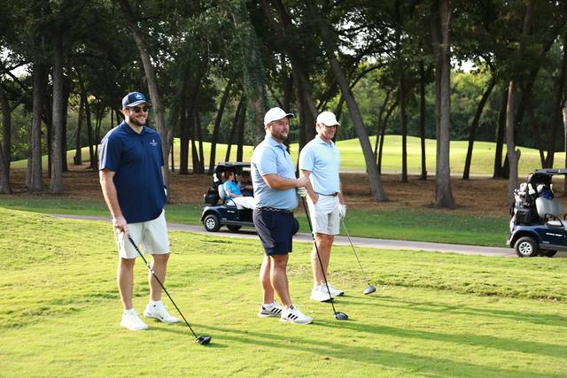Three players talking on the tee beside the cart path