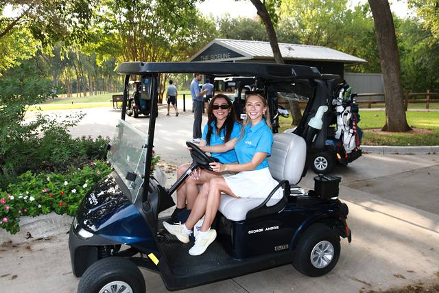 Two women in MCBA shirts driving a cart