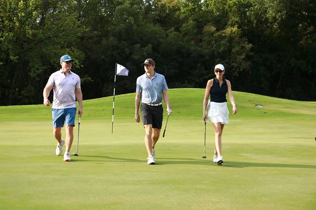 Three players walking off a green past a Cowboys flag