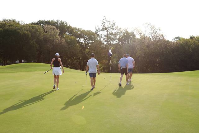 A group walking up to a green in the morning light