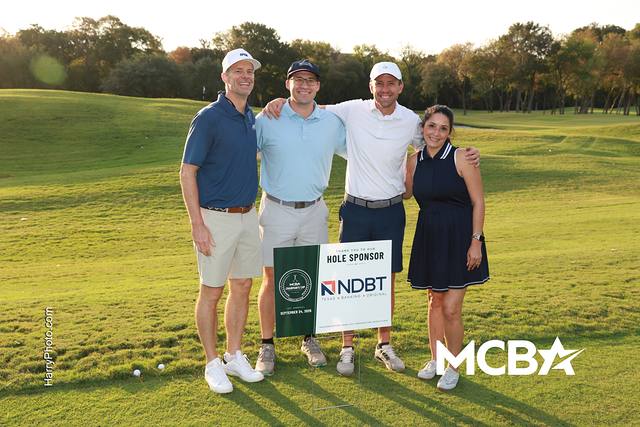A group smiling beside the North Dallas Bank & Trust hole sponsor sign