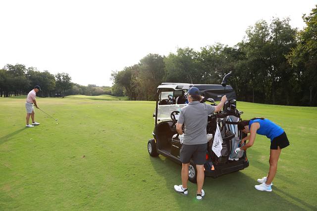 Two players at their cart on the fairway as another hits
