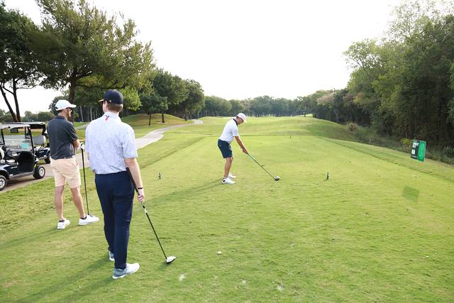 A player teeing off down a long fairway while his partners watch