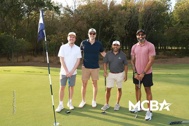 A group smiling beside the flag on a green