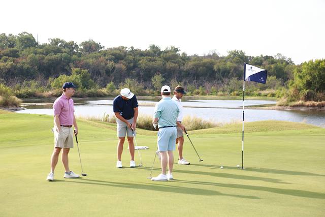 A group around the flag on a green with a pond behind it