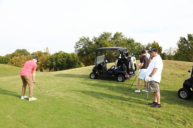 A player chipping toward the green while his partners wait by the carts