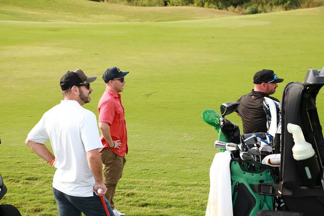 Three players waiting by their cart on the fairway