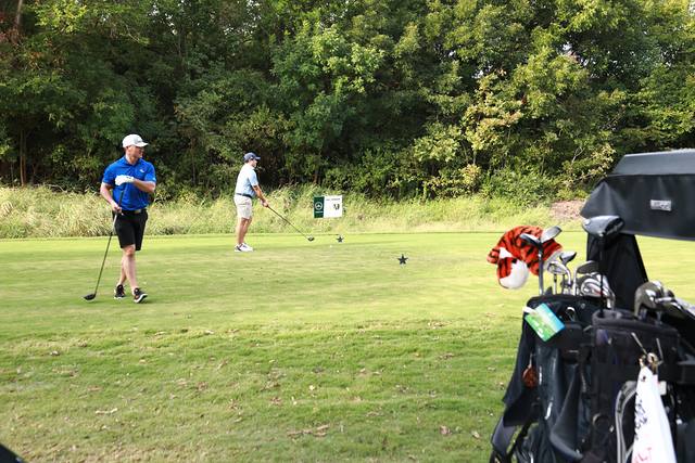 A player teeing off seen past a cart full of golf bags