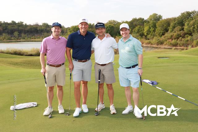 A group posing on a green with water behind them