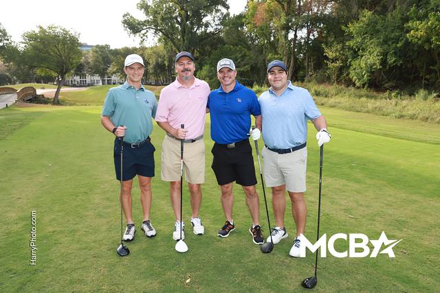 A group smiling on a tee box with trees behind them