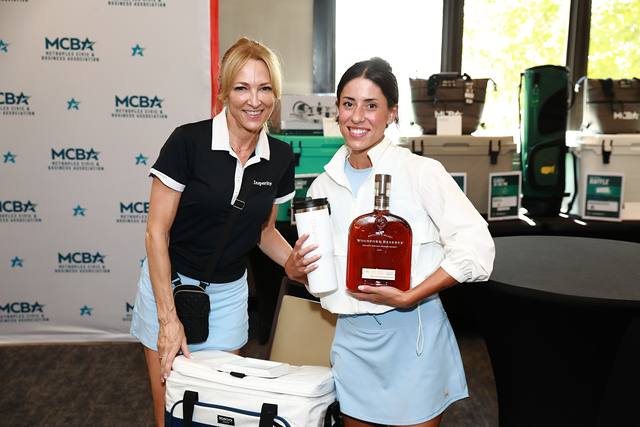 Two guests with a bottle of bourbon and a cooler at the prize table