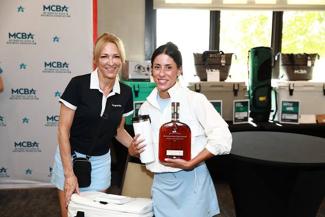 Two guests smiling with a bottle of bourbon at the prize table