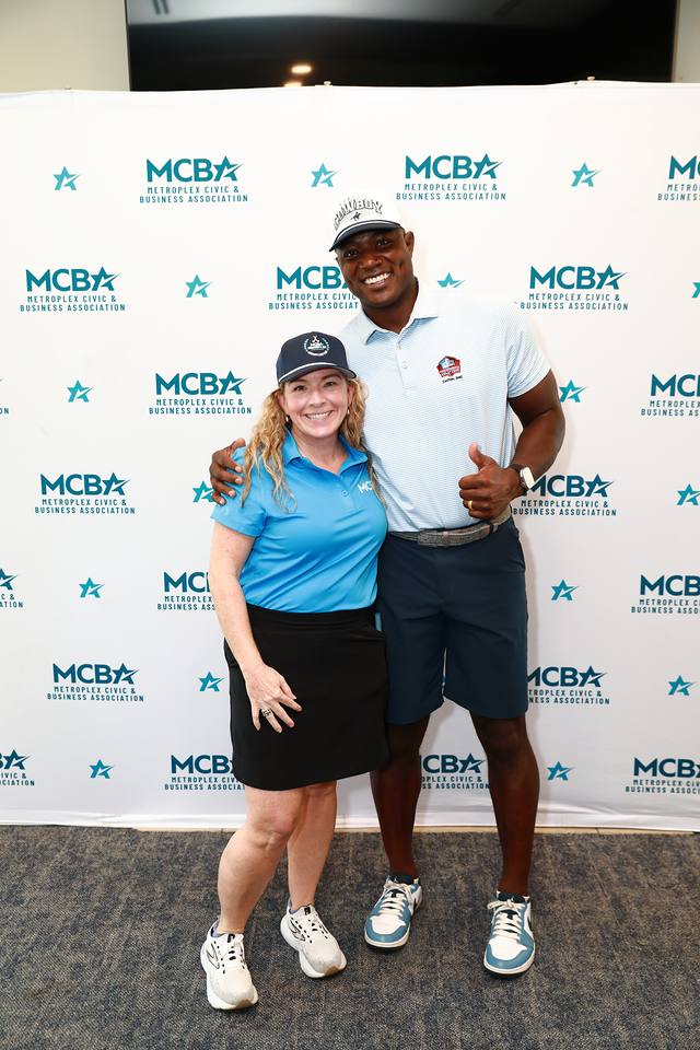 An MCBA team member posing with a guest in front of the MCBA backdrop