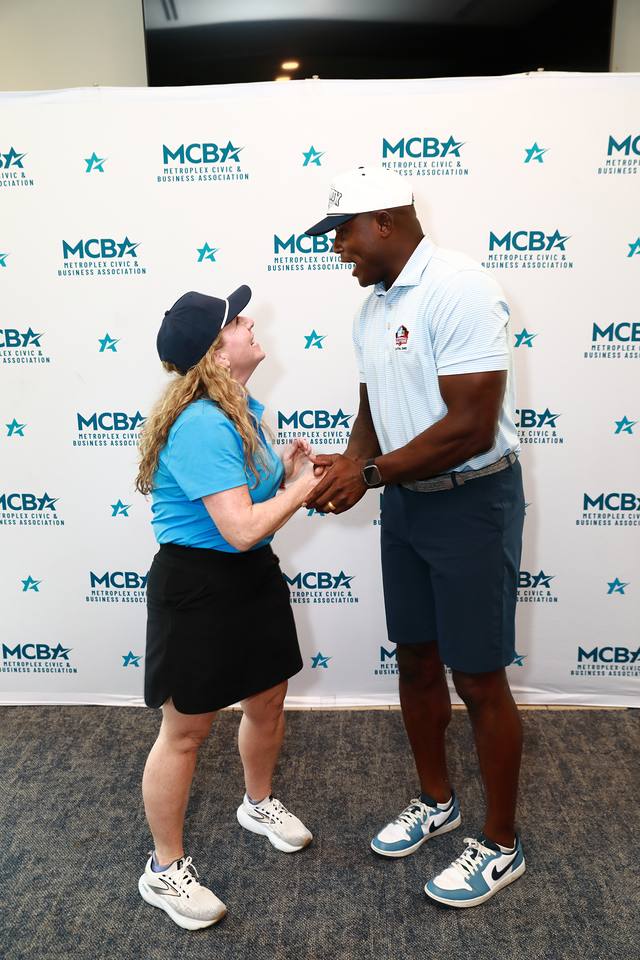 An MCBA team member shaking hands with a guest at the MCBA backdrop