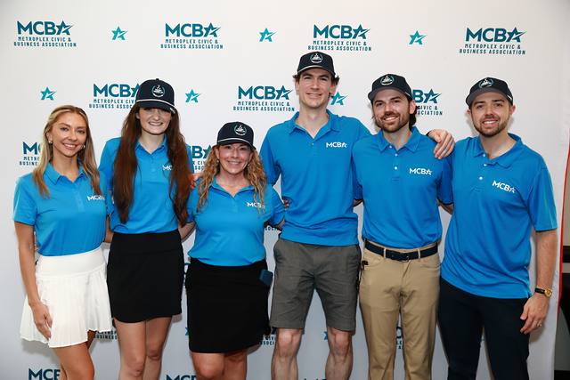 The MCBA team smiling in front of the backdrop